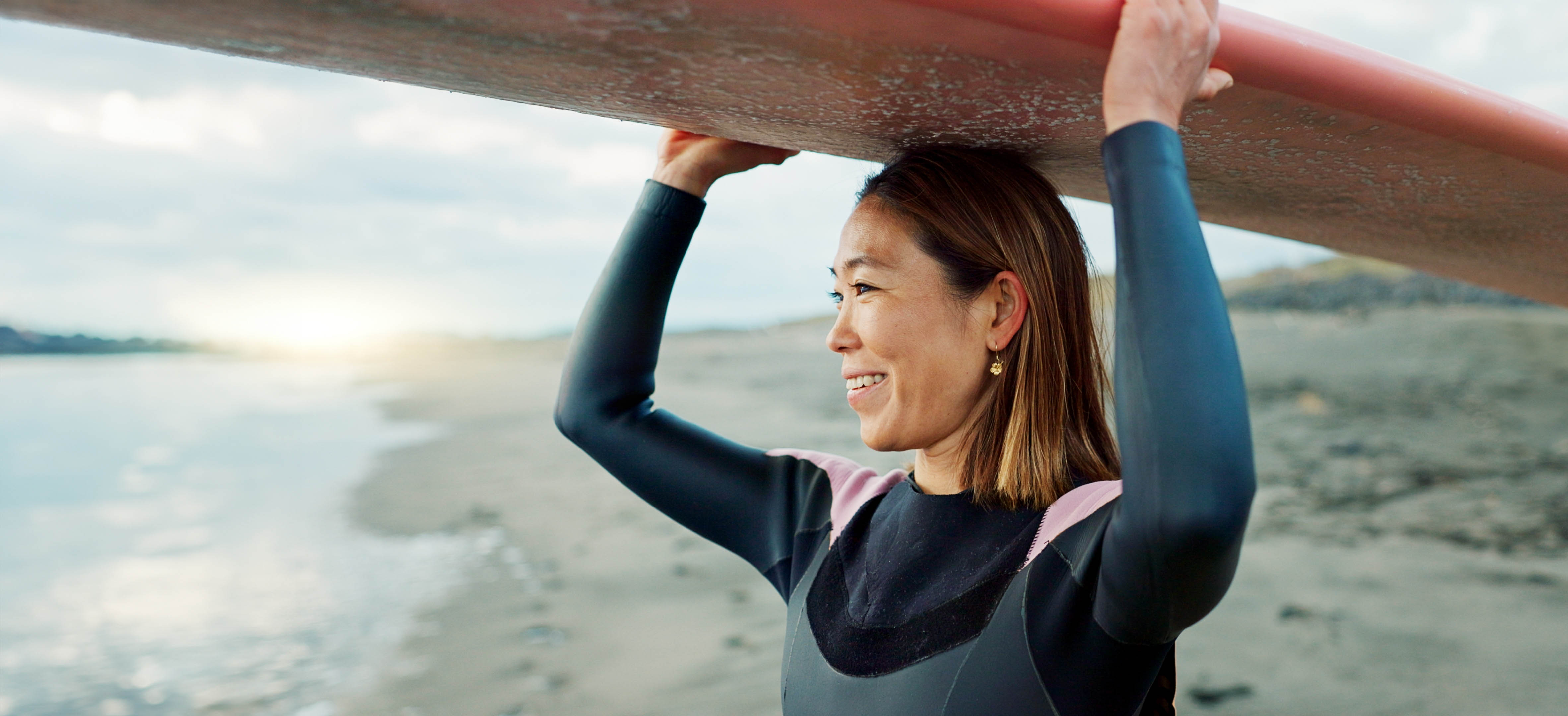 Older woman, smiling looking out to the ocean, with a surfboard on her head Older woman, smiling looking out to the ocean, with a surfboard on her head